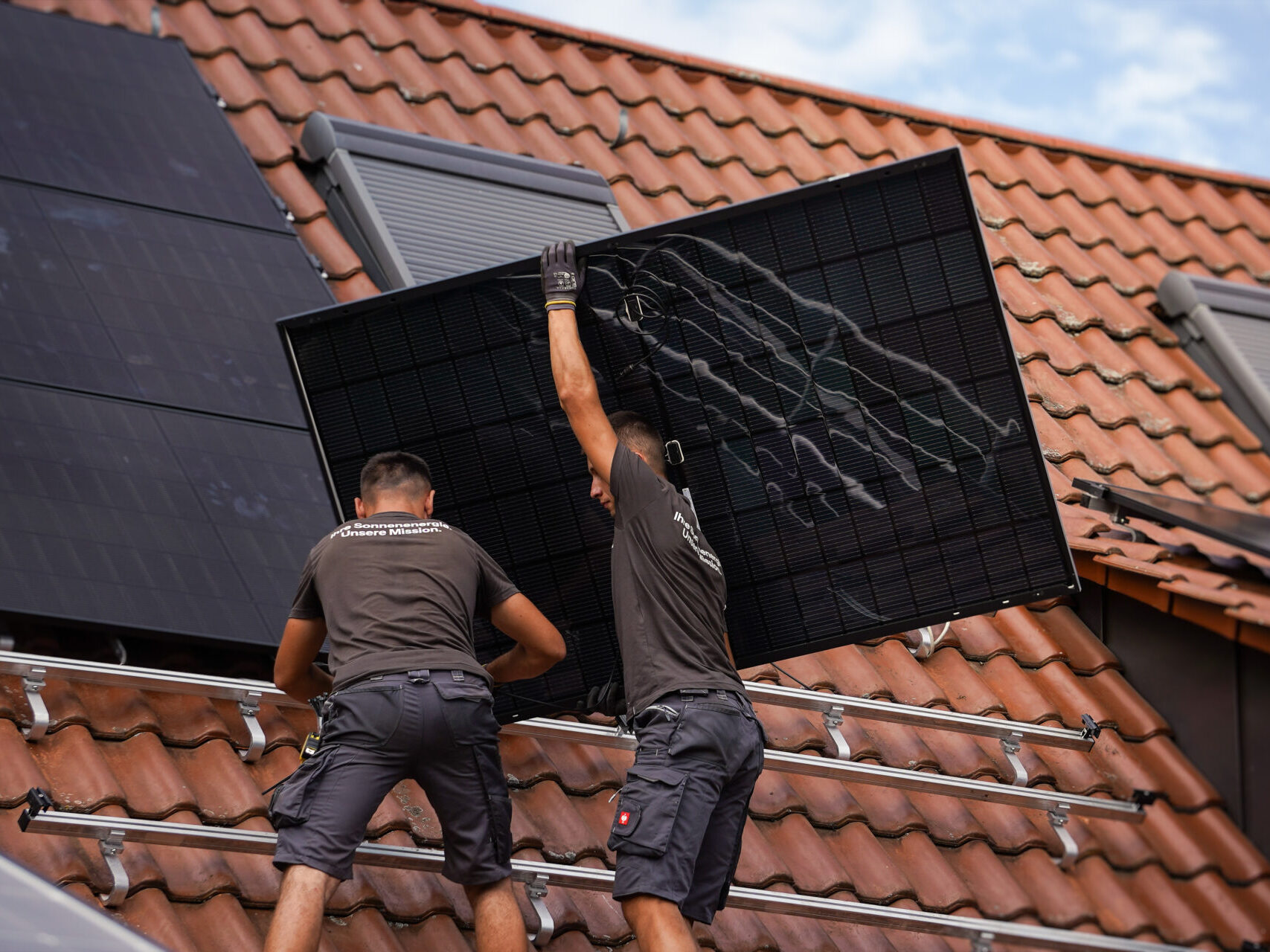 Zwei Mitarbeiter belegen ein Dach mit PV-Modulen