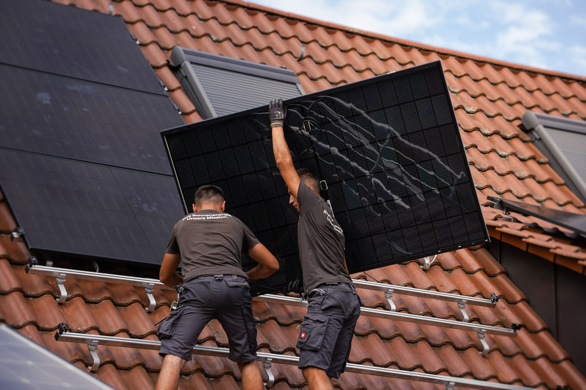 Zwei Mitarbeiter belegen ein Dach mit PV-Modulen